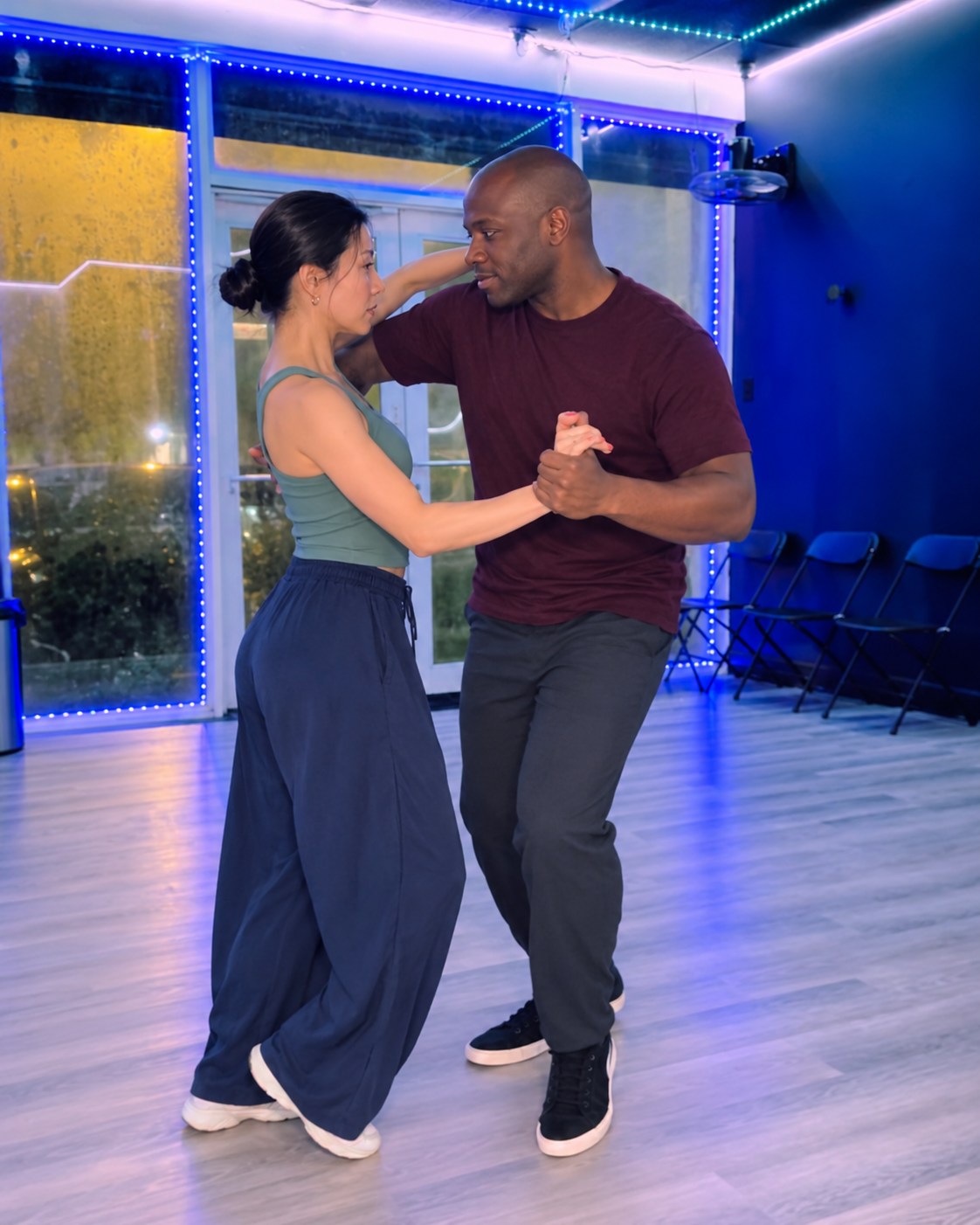 Two partners dancing together in a blue-lit social dance studio.